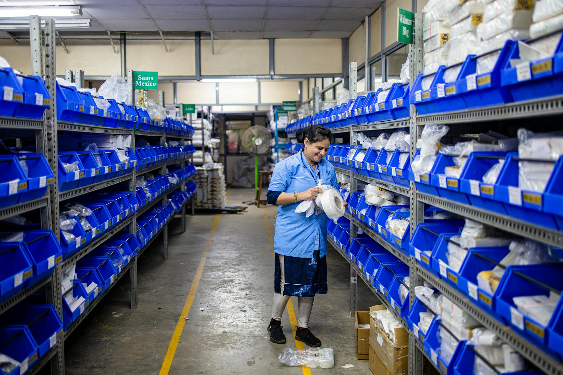 Pracownica porządkuje towar między regałami magazynu z niebieskimi pojemnikami