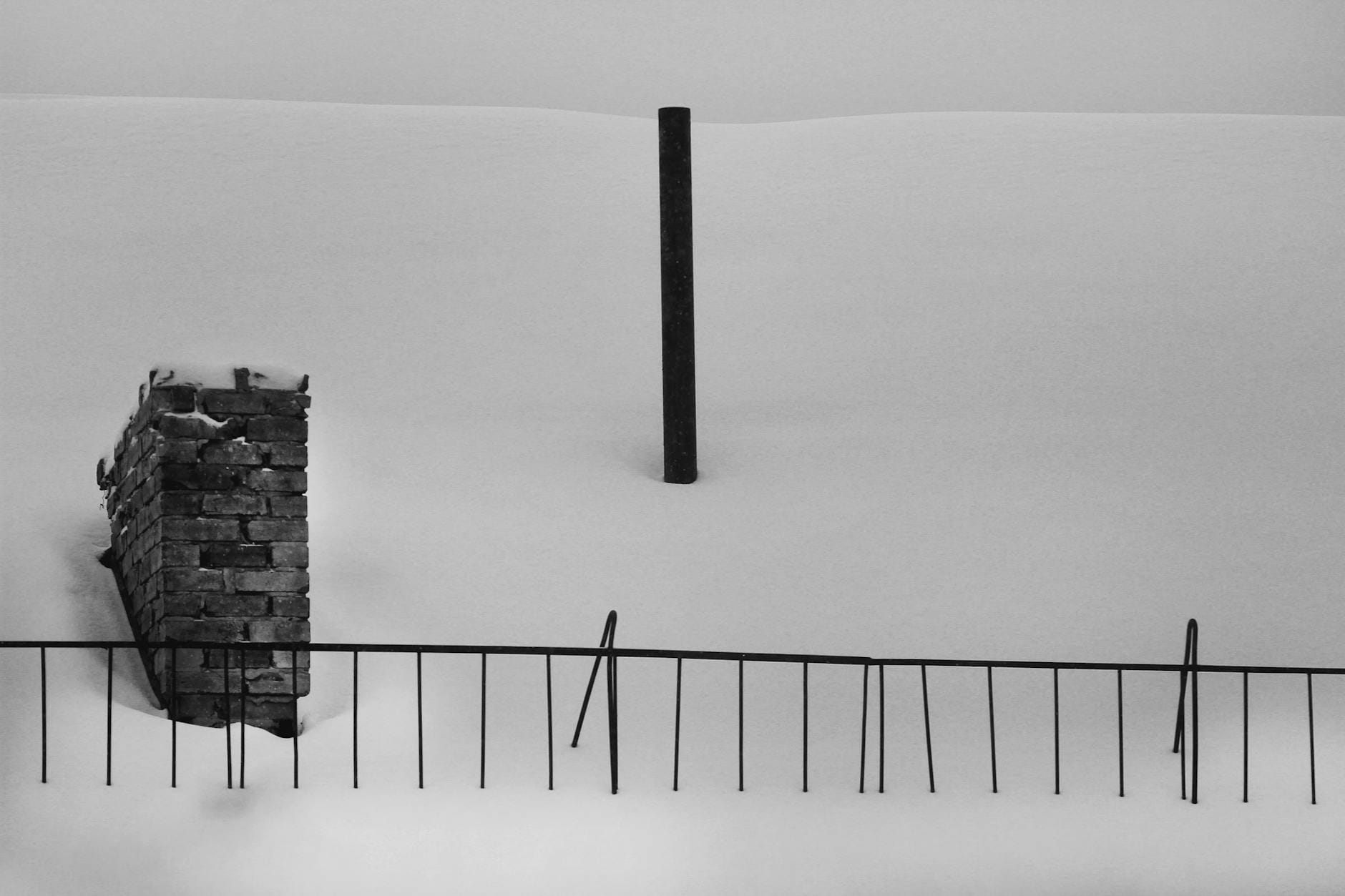Czarno-białe ogrodzenie i ceglana ściana w ośnieżonym krajobrazie