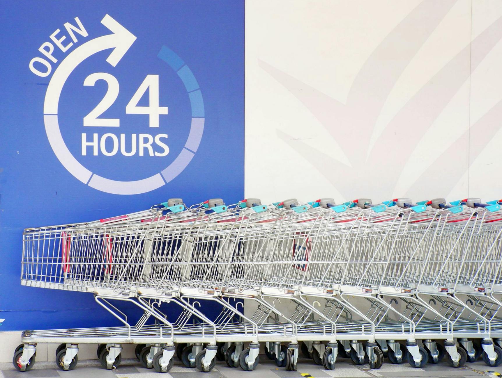 Rząd metalowych wózków sklepowych przed całodobowym supermarketem