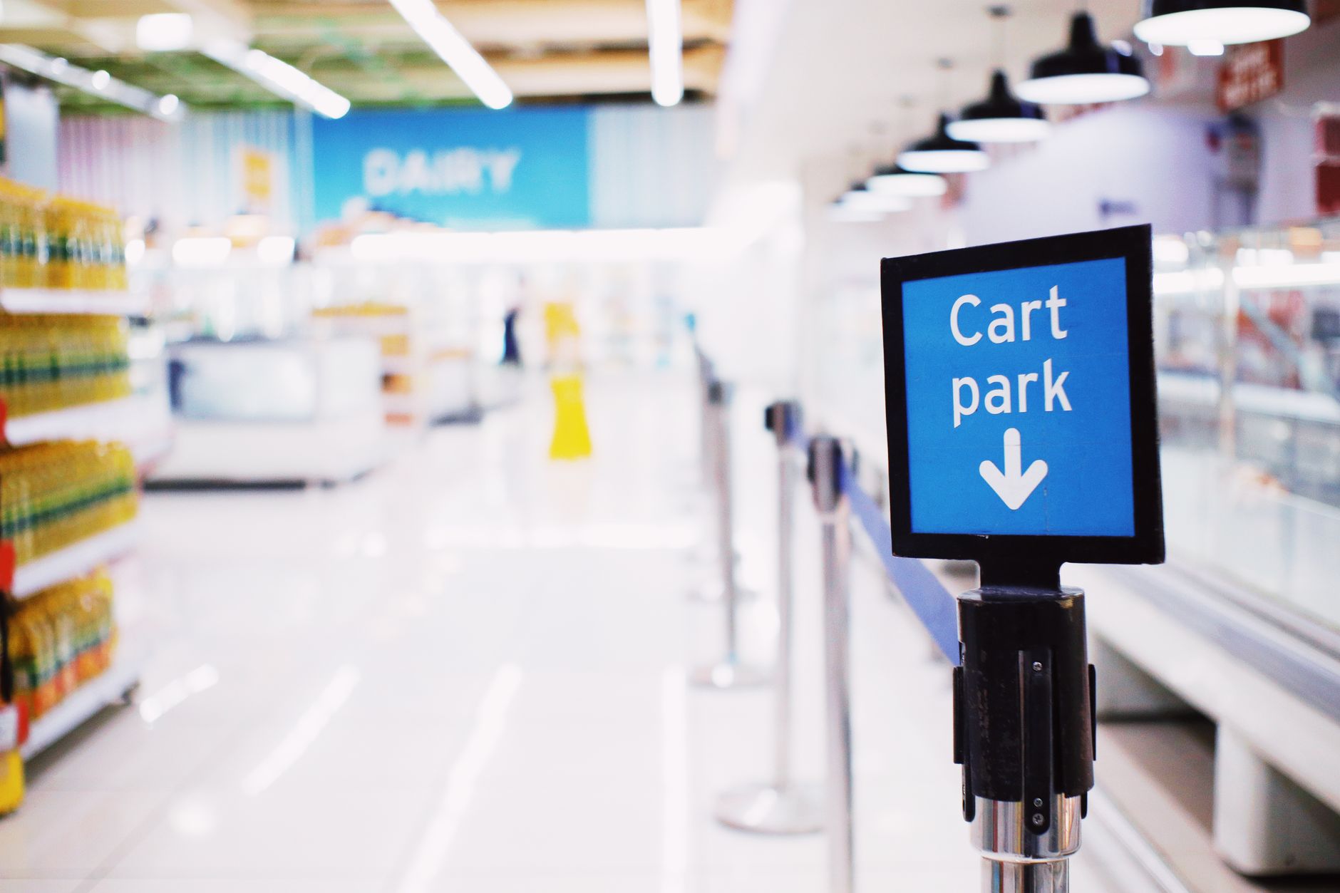 Jak projektować alejki sklepowe, aby uniknąć zatorów, kolizji i niebezpiecznych sytuacji Niebieski znak Cart park przy kasie w nowoczesnym supermarkecie